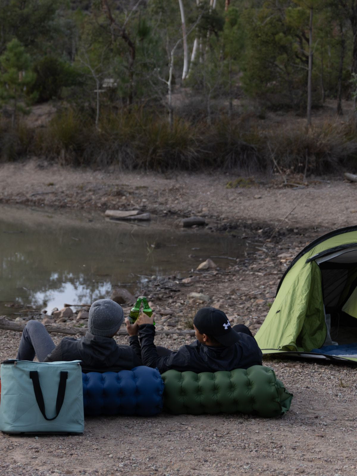 4 personnes en camping sur leurs matelas Le P'tit Nomad entrain de trinquer au bord d'un lac.